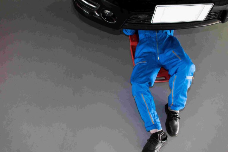 Mechanic,in,blue,uniform,lying,down,and,working,under,car